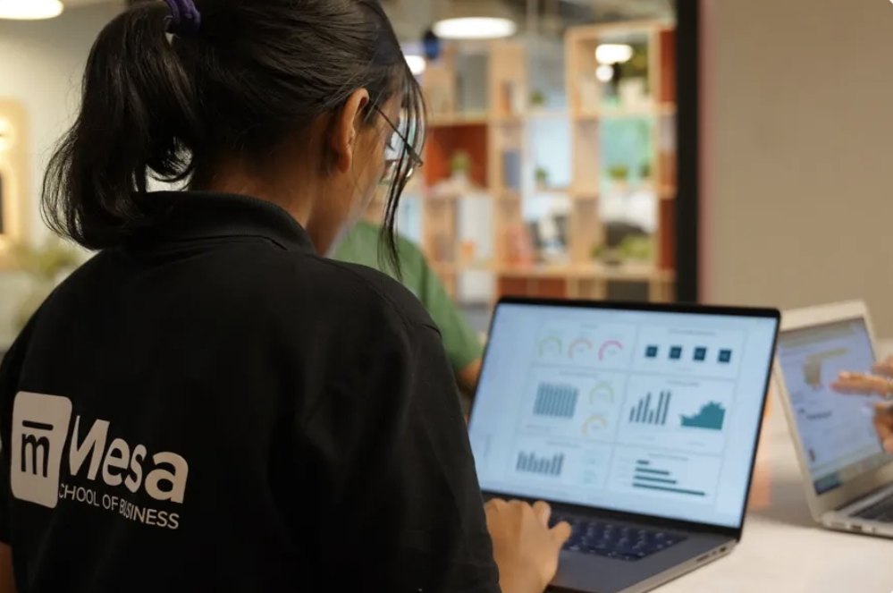 A student in a Mesa t-shirt building a dashboard on a laptop